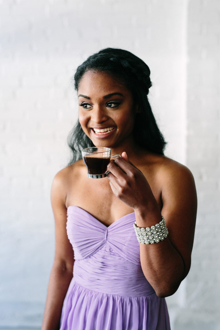 Young woman in a strapless lavender dress sipping on a clear mug of coffee