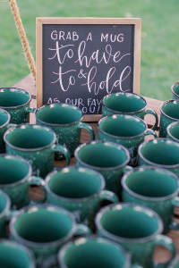 Green custom reusable coffee mugs on table with sign saying Grab a Mug
