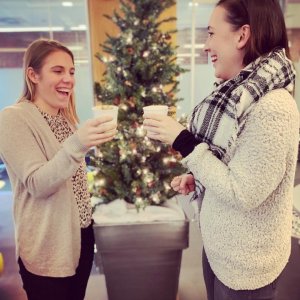 Two women drinking cappuccinos in front of a Christmas tree during an Espresso Dave's Coffee Catering office holiday party in Boston.