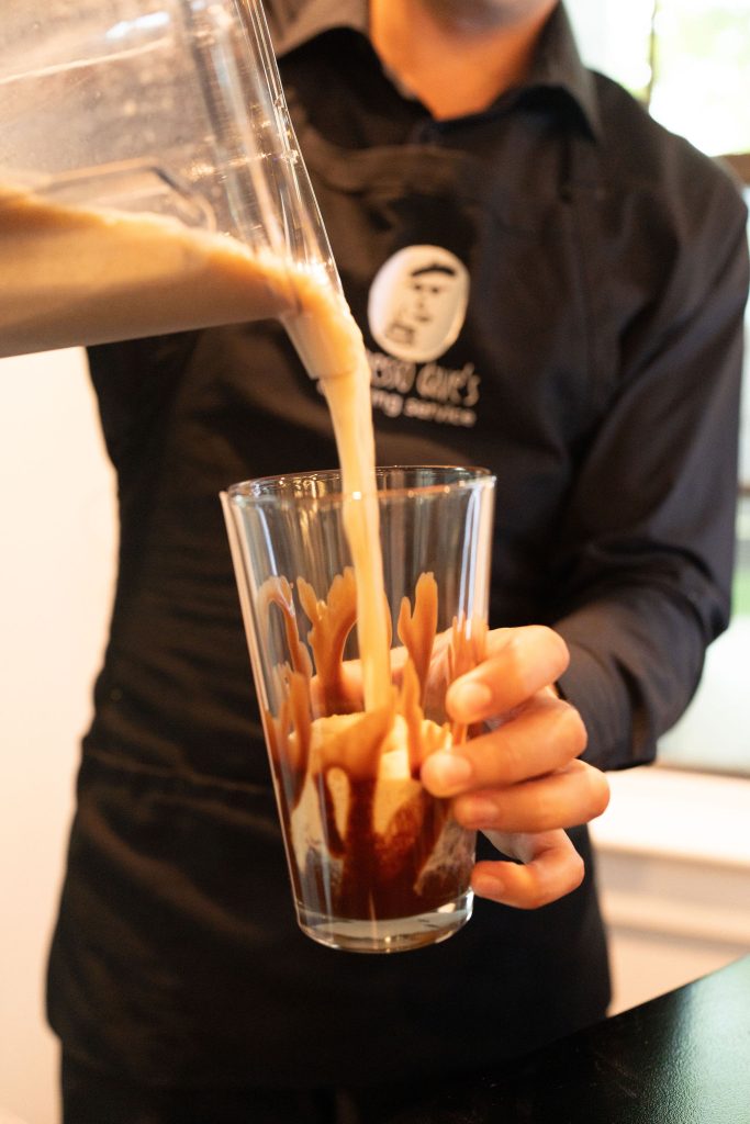 Espresso Dave Barista in black uniform pouring frozen coffee drink into large glass with drizzled chocolate for alcohol free events